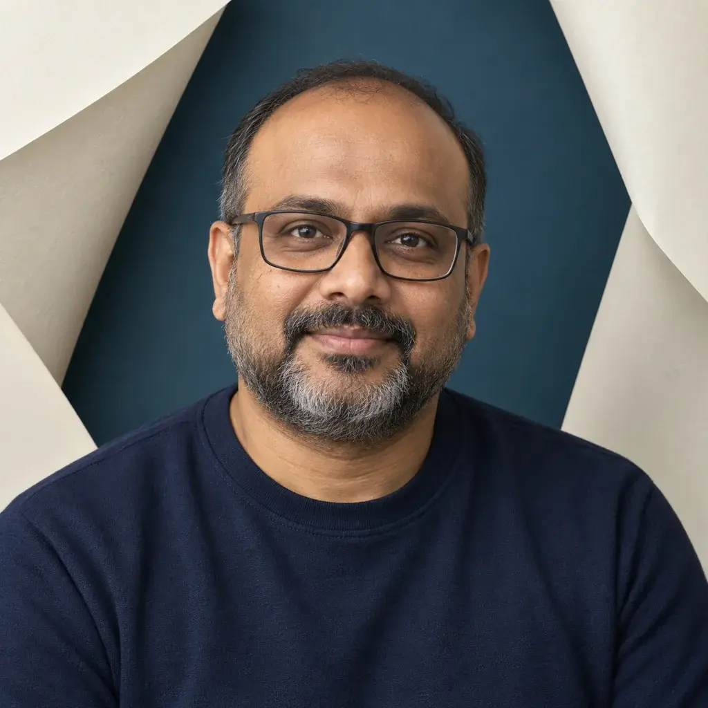 A man with glasses and a salt-and-pepper beard framed by folded cream paper against a blue background.